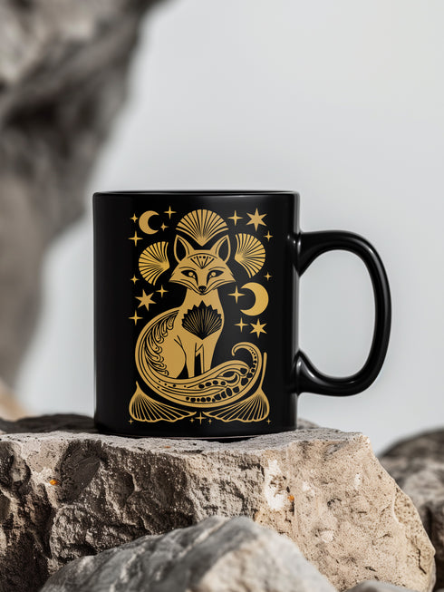 A black ceramic mug featuring a stylized golden fox design surrounded by Art Deco ginkgo fans, crescent moons, and stars. The mug has a glossy finish and ergonomic handle.